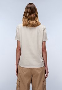 Beige katoenen t-shirt met korte mouwen, iets ontspannen pasvorm, naaddetails en een ronde hals, gecombineerd met lichtbruine cargobroek.