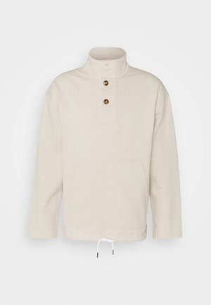 Maglione beige chiaro con collo alto, due bottoni, tasca frontale a marsupio e coulisse bianca all'orlo.