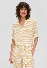 Beige Oberteil mit weißen Zebra-Streifen, V-Ausschnitt, kurzen Ärmeln, lockerer Passform, kombiniert mit passenden Hosen mit gebundenem Bund und Taschen.