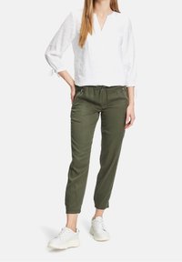 White linen blouse with three-quarter sleeves and a v-neck, paired with olive green tapered pants featuring side zip pockets and drawstring.