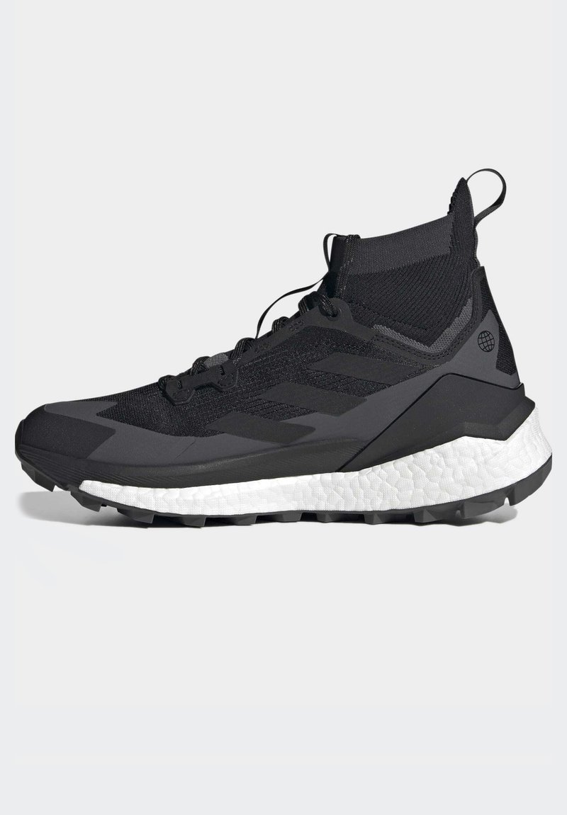 Schwarzer Sportschuh mit einem strukturierten, gestrickten Obermaterial, ausgestattet mit einer weißen Zwischensohle und einer schwarzen Außensohle. Enthält Schnürsenkel und eine Zugschlaufe an der Ferse.