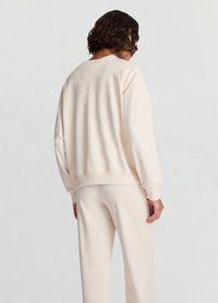 Sweat-shirt beige clair à coupe décontractée, manches raglan et poignets côtelés. Texture lisse, design minimaliste sans motifs visibles.