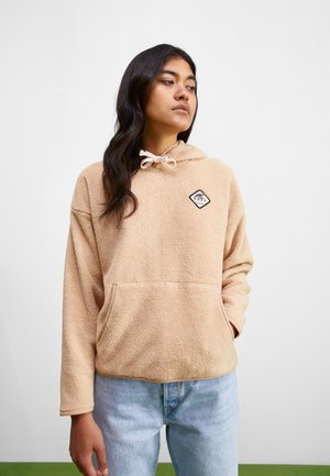 Beige fleece huppari, jossa on etutasku ja timantinmuotoinen logo rinnassa. Varustettu kiristettävällä hupulla ja rentolla istuvuudella.
