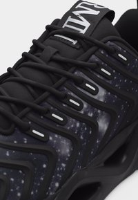 Μαύρο αθλητικό παπούτσι με ύφασμα σε σχέδιο γαλαξία, χοντρές μαύρες κορδόνια και έντονες μαύρες επενδύσεις κατά μήκος της πλευράς και της γλώσσας.