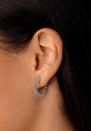 Orecchini a cerchio in argento con un design spigoloso, caratterizzati da piccole accentuazioni di perle lungo il bordo esterno, che mettono in mostra una finitura metallica lucida.