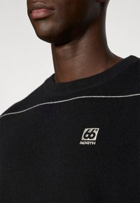 Maglione nero a maglia con scollo rotondo, dotato di una linea bianca di accento e un piccolo logo ricamato nell'angolo in basso.