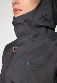 Dark gray waterproof jacket with a high collar, zipper closure, and logo details. Features adjustable strings and a textured fabric.