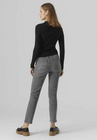 Top de manga larga negro de canalé combinado con jeans ajustados grises. El modelo lleva zapatos de plataforma negros. Diseño simple, detalles de costura sutiles.