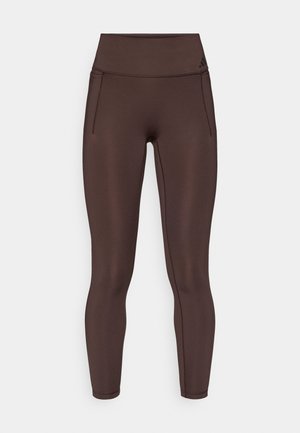 Bruine sportlegging met een hoge tailleband, een gladde textuur en onopvallende zijzakken. Voorzien van subtiele zwarte branding vlak bij de tailleband.