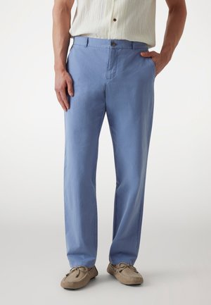 Pantalon en coton bleu clair à jambe droite, avec une fermeture à un bouton et des poches latérales, associé à des mocassins beiges.