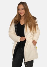 Longue doudoune crème avec intérieur noir, poignets élastiques, taille ajustable et fermeture éclair frontale. Deux poches latérales avec fermetures éclair contrastantes.