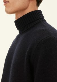 Maglione lavorato a maglia di colore navy con collo alto a costine, realizzato in materiale morbido, caratterizzato da una silhouette relax e una superficie testurizzata.