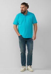 Türkises Poloshirt, kurze Ärmel, aus Baumwollmaterial. Kombiniert mit dunkelblauen Jeans und weißen Sneakern. Einfaches Design, keine sichtbaren Muster oder Logos.