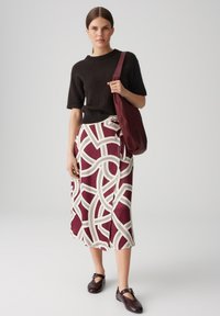 Pull à manches courtes en tricot noir, associé à une jupe midi maroon et blanche à motifs géométriques, et des chaussures plates marron.
