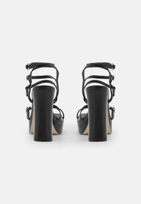 Sandalias negras de tacón alto con un chunky block heel, múltiples tiras delgadas y hebillas ajustables en el tobillo. Textura de cuero suave.