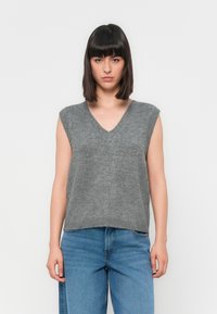 Grijze mouwloze trui met een V-hals ontwerp, gebreide textuur en een losse pasvorm, gecombineerd met lichtblauwe denim jeans.