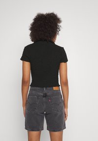Black textured crop top with a collar, paired with high-waisted, faded gray denim shorts, featuring back pockets and a brand label.