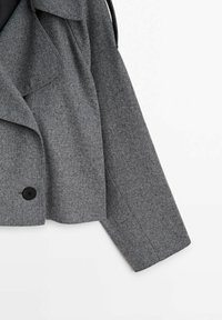 Manteau court en laine grise avec manches longues, larges revers et un seul bouton noir en bas à l'avant.