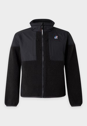Casaco polar preto com fecho de correr e painéis de tecido liso nos ombros e peito, com pequeno logótipo azul, vermelho e branco no lado esquerdo do peito.