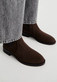 Brune suedet Chelsea-støvler med elastiske sidepaneler, rund tå og en teksturert såle. Kombinert med lysegrå, løstsittende jeans.