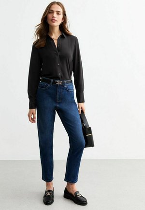 Black button-up shirt, dark blue jeans, black loafers, and black handbag. Features include a sleek design and metallic belt buckle detail.