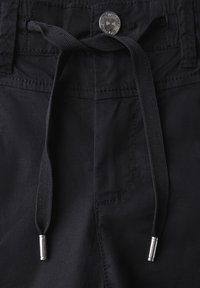 Pantalones negros con cierre de cordón y puntas de metal plateado, textura suave y detalle de costura en los bolsillos frontales.