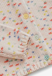 Cardigan en tricot rose clair avec motif zigzag multicolore et boutons pastel jaunes, verts et bleus, présenté plié au niveau de la manche.