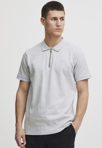 Grå polo shirt med en kort lynlåskrave, lavet af blødt stof, med korte ærmer og en diskret logo detalje på brystet.
