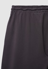 Dunkelgraue Sporthose mit einem elastischen Bund, glatter Textur und einer Seitentasche. Schlichtes Design ohne Muster oder Verzierungen.