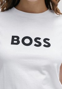 Vit bomull t-shirt med fet svart "BOSS" text över bröstet. Klassisk crew neck-design med mjuk textur.