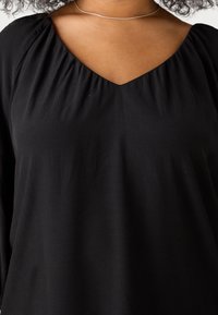 Blusa nera con scollatura a V e dettagli arricciati sulle spalle. Realizzata in tessuto morbido con una trama liscia e una vestibilità comoda.