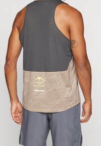 Bezrękawnik sportowy w kolorze ciemnoszarym i beżowym. Posiada teksturowaną siateczkową górę, wzorzystą dolną część oraz logo w kolorze żółtym.