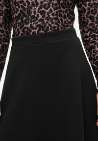 Černá sukně se strukturovaným páskem a volným siluetem, kombinovaná s dlouh�ým rukávem topem s fialovým leopardím potiskem. Hladká textura.