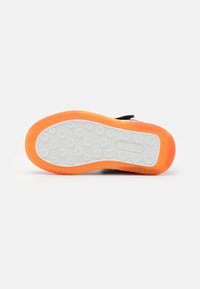 Suela de zapato negra con una base blanca y acentos naranjas. Presenta patrones circulares texturizados para agarre y una sección suave en el medio.