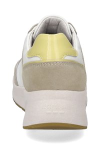 Weiße und beigen Sneaker mit einer strukturierten Wildleder-Ferse, glänzenden gelben Akzenten und einer weißen Gummisohle. Branding auf der Ferse sichtbar.