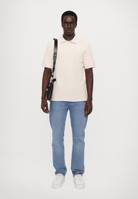 Beige poloskjorte med krage, blå denimjeans, hvite sneakers og en svart crossbody-veske. Enkelt design, tettsittende silhuett og avslappet stil.