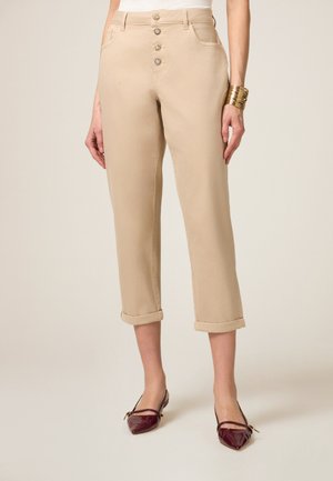 Pantalons cropped beiges avec ourlets roulés, fermeture à cinq boutons à la taille, et poches avant ; le tissu semble lisse avec une texture douce.