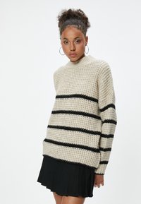 Chunky gestrickter Pullover in Beige mit schwarzen horizontalen Streifen, hohem Kragen und lockerer Passform. Strukturierter Stoff mit gerippten Ärmeln und Saum.