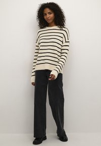 Maglione a righe crema e nero con vestibilità ampia, maniche lunghe e polsini a coste, abbinato a jeans neri a vita alta e scarpe nere.