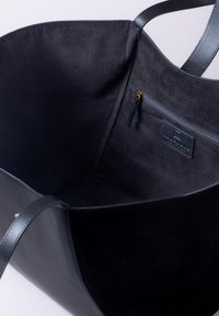 Black tote bag with leather and suede texture, open interior, interior zipped pocket with a leather pull tab, smooth straps.