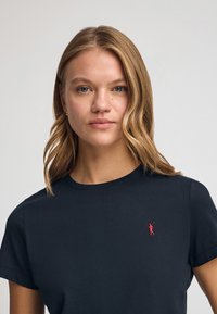 Granatowa bawełniana koszulka z okrągłym dekoltem i krótkimi rękawami, z małym czerwonym emblematem golfisty po lewej stronie na klatce piersiowej. Gładka struktura.