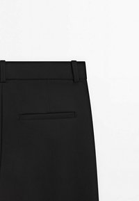 Pantalon noir avec une texture lisse, coupe droite, taille simple et une poche arrière unique. Pas de motifs ou de matériel visibles.