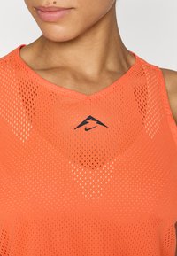 Débardeur d'athlétisme en maille orange avec un design en V et un logo Nike noir sur la poitrine, mettant en valeur un tissu respirant avec des détails texturés.