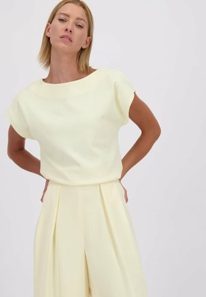 Blouse côtelée jaune clair avec un décolleté bateau et des manches courtes, associée à un pantalon jaune clair à large jambe et plis. Texture lisse.