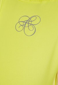 Tejido de rendimiento amarillos con textura de ribete fino. Presenta un logo estilizado gris en el centro. No hay patrones adicionales ni herrajes visibles.