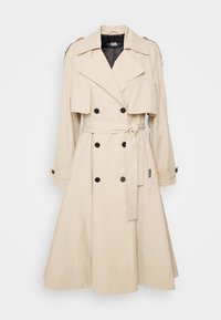 Trench-coat beige à double boutonnage avec larges revers, ceinture ajustable, poignets à boutons et épaulettes.