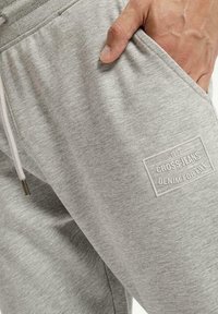 Szare dresowe spodnie z miękkiego materiału, z boczną kieszenią, wiązanym w pasie oraz prostokątną białą naszywką z logo "CROSS JEANS".
