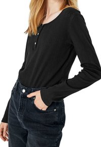 Svart långärmad topp med ribbad textur, rundad halsringning och tre knappslå. Matchas med högmidjade mörka jeans.