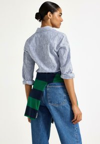 Stribet skjorte med opsmøgte ærmer, parret med højhalsede blå jeans. En grøn og marineblå stribet sweater bundet om taljen.