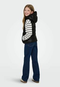 Crna puffer prsluk s kapuljačom nosi se preko bijele i crne prugaste košulje dugih rukava. Uparen s plavim trapericama i laganom obućom.